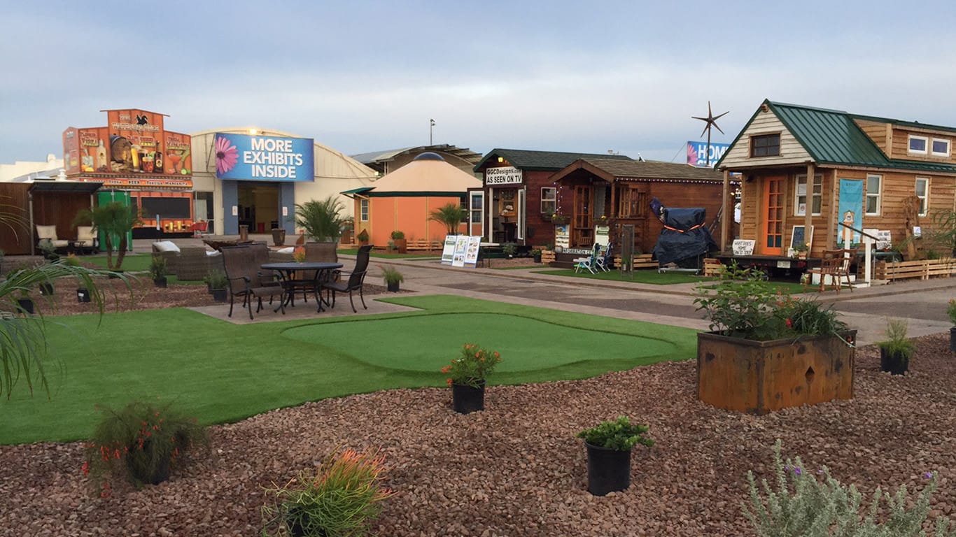 Home and Garden Show exhibit featuring various outdoor displays, including tiny homes, seating areas, and landscaping elements, set in a vibrant, garden-like atmosphere.