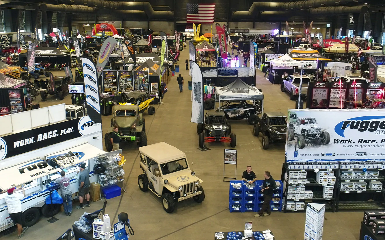 Indoor setting of All Things Outdoor Expo featuring various vendor booths, off-road vehicles, and promotional banners, showcasing outdoor gear and activities, with attendees engaging and exploring the event.
